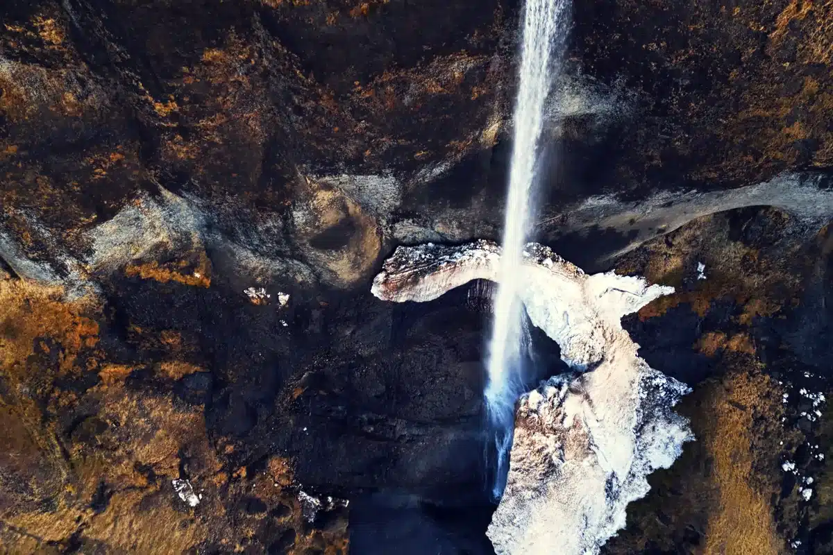 Vista aérea de una cascada que cae entre rocas oscuras con hielo y nieve