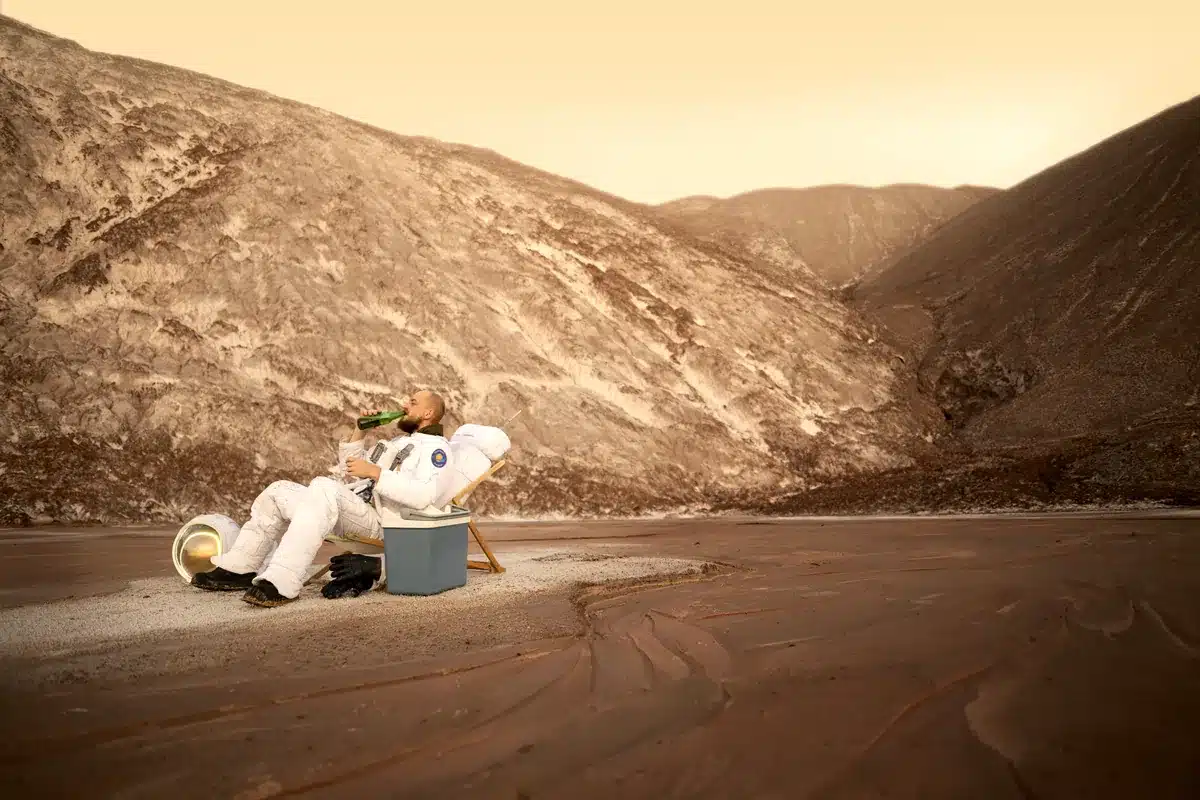 Fotomontaje de un astronauta que descansa en una silla de playa junto a una nevera portátil en un valle desértico