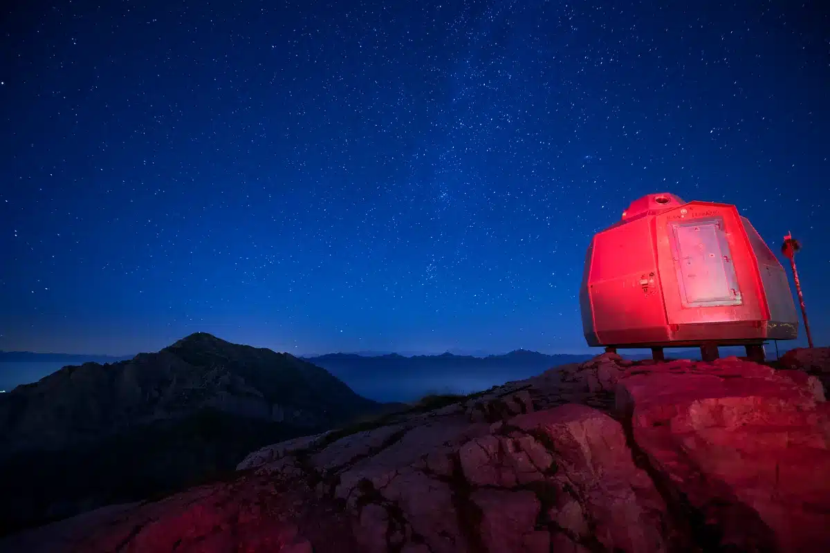 Refugio de montaña rojo sobre una roca bajo un cielo nocturno estrellado