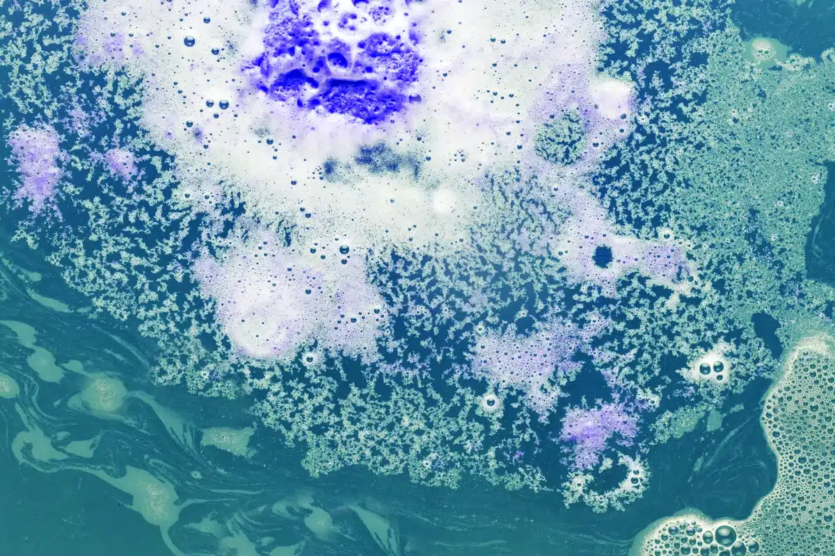 Imagen abstracta de manchas blancas y violetas sobre un fondo turquesa, como vista al microscopio
