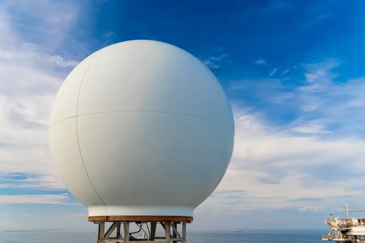 Gran cúpula esférica blanca sobre una base metálica, frente al mar y un cielo con nubes