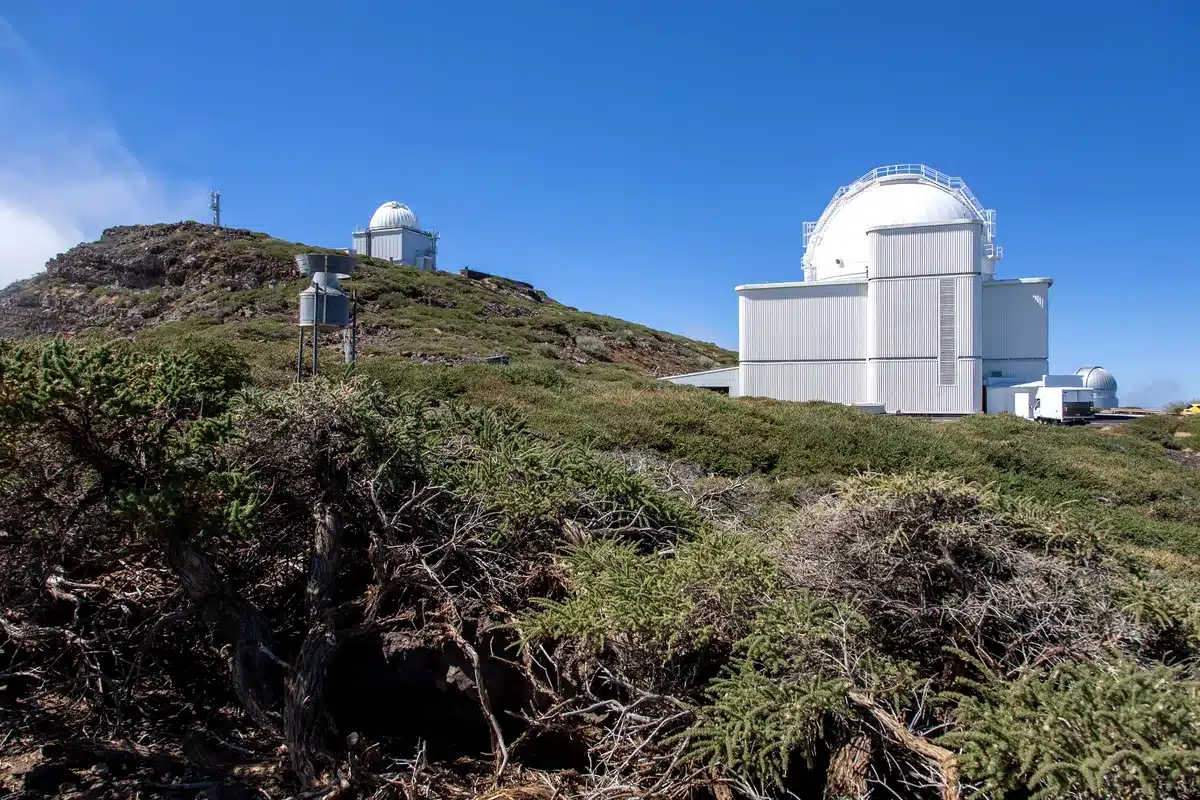 Observatorio de cúpula blanca en la cima de una montaña con vegetación baja y cielo despejado