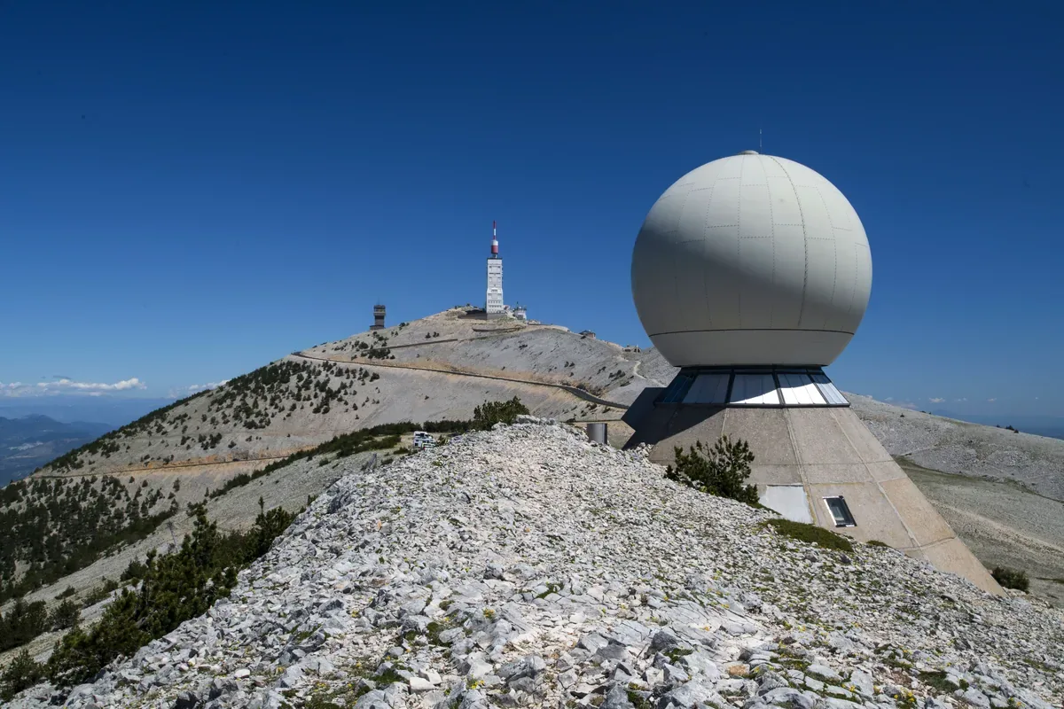 Cúpula blanca de un radar junto a una torre en la cima pedregosa de una montaña