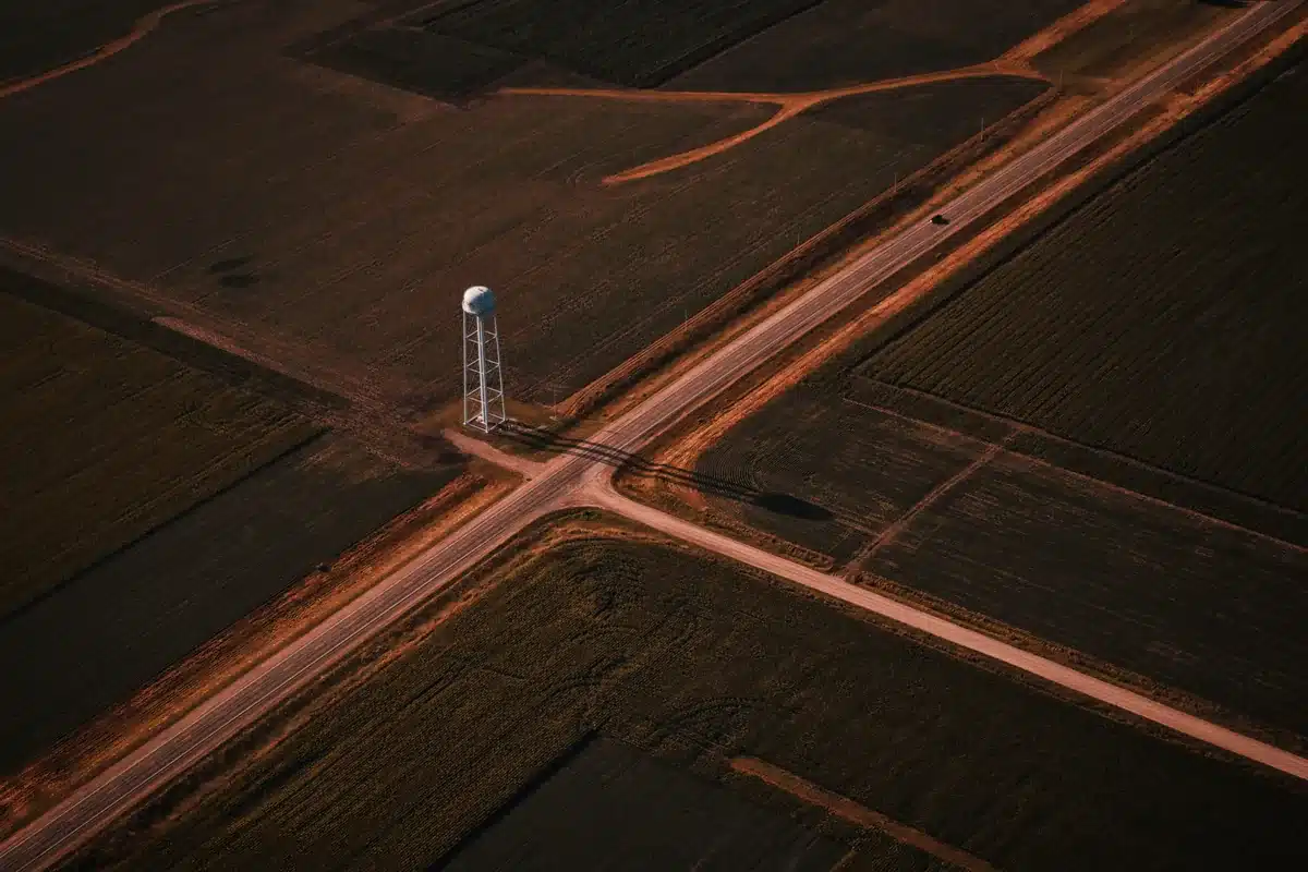 Vista aérea de un cruce de caminos rurales entre campos, con un tanque de agua elevado