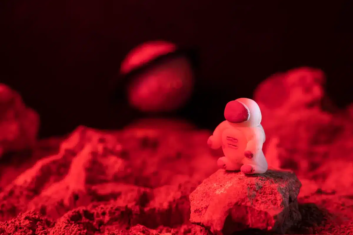 Figura de juguete de un astronauta sobre rocas iluminadas de rojo, con un planeta desenfocado al fondo