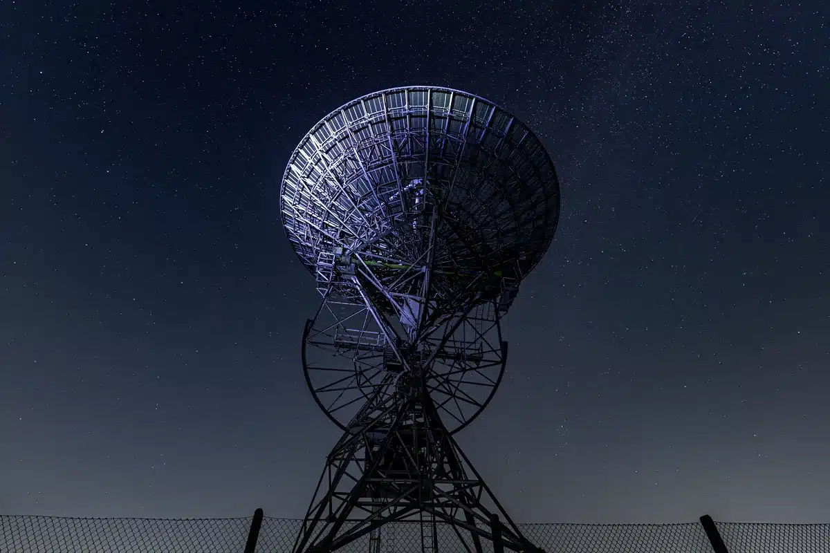 Antena de radiotelescopio vista desde abajo contra un cielo nocturno estrellado