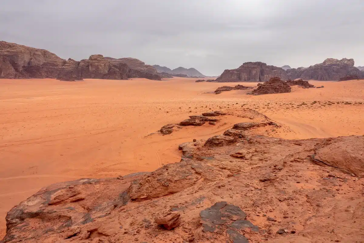 Desierto de arena rojiza con formaciones rocosas bajo un cielo nublado