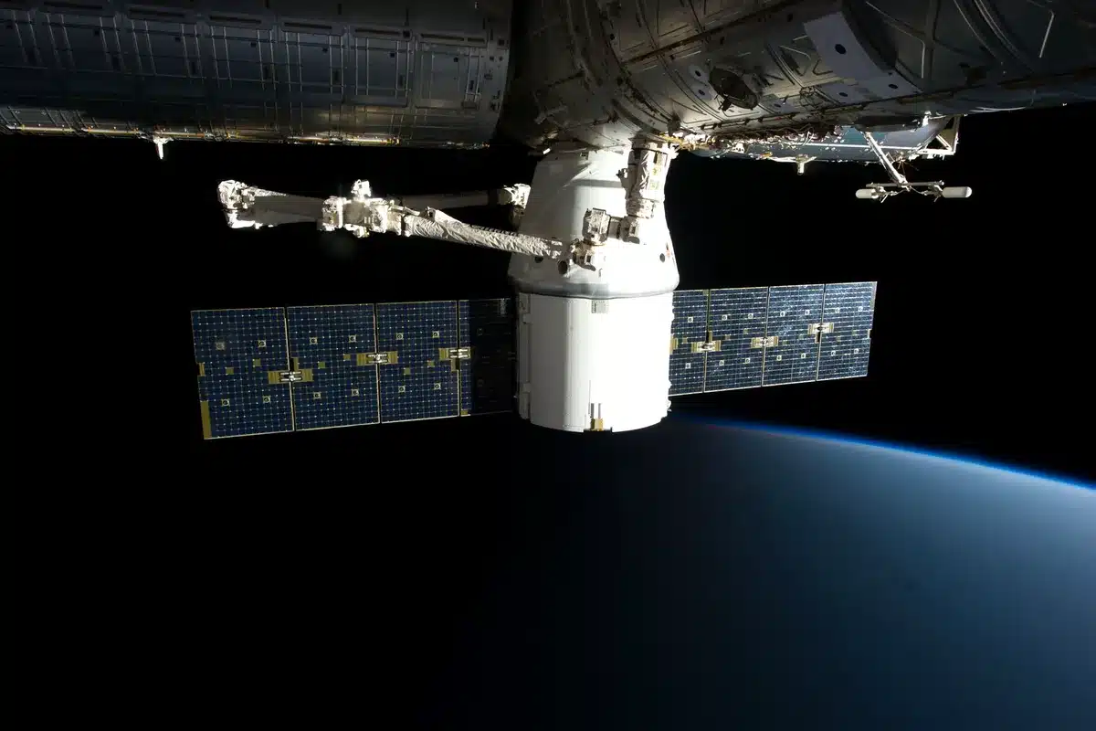 Brazo robótico de la Estación Espacial Internacional que sujeta una cápsula de carga sobre la Tierra