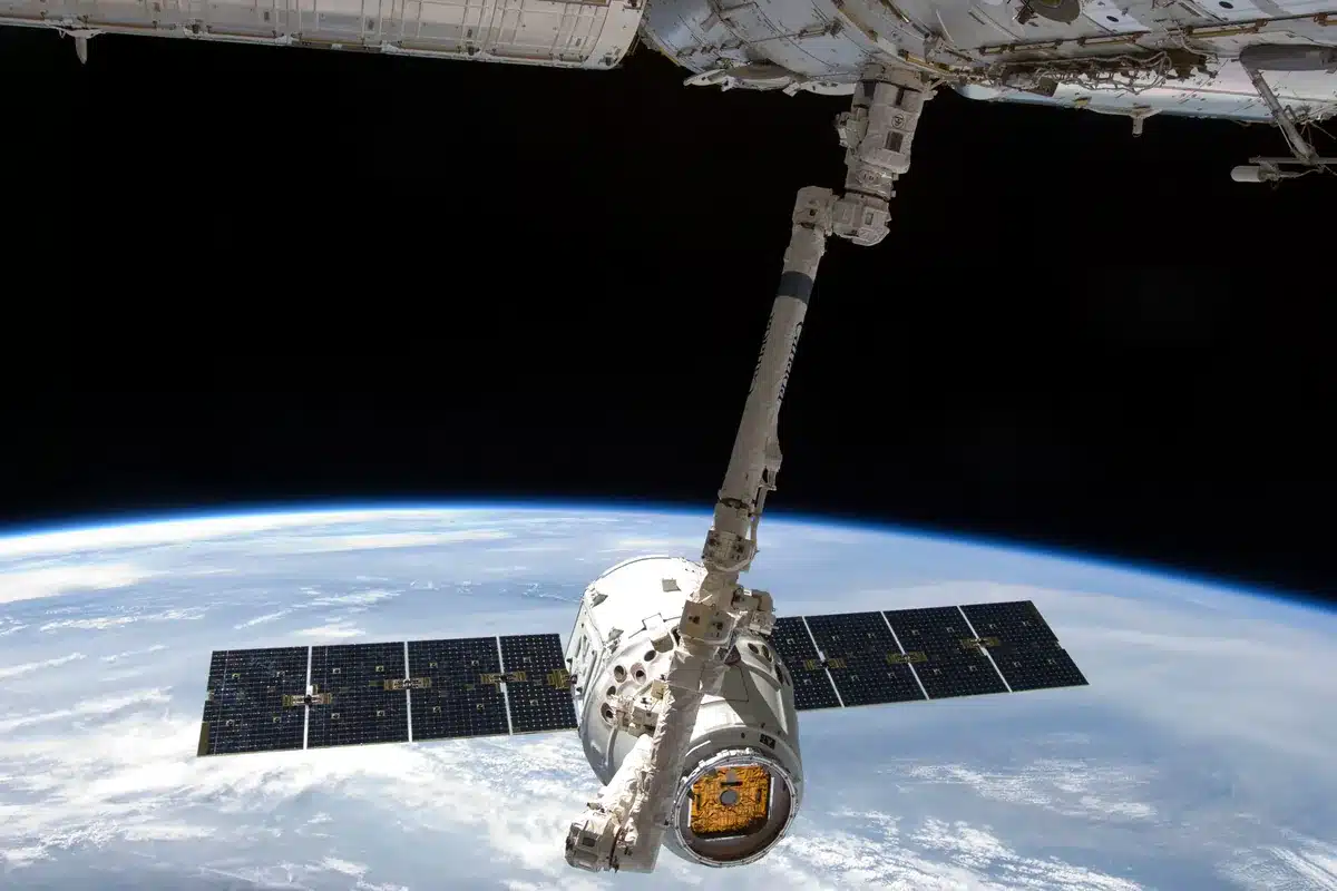 Brazo robótico de la Estación Espacial Internacional que sujeta una cápsula de carga sobre la Tierra