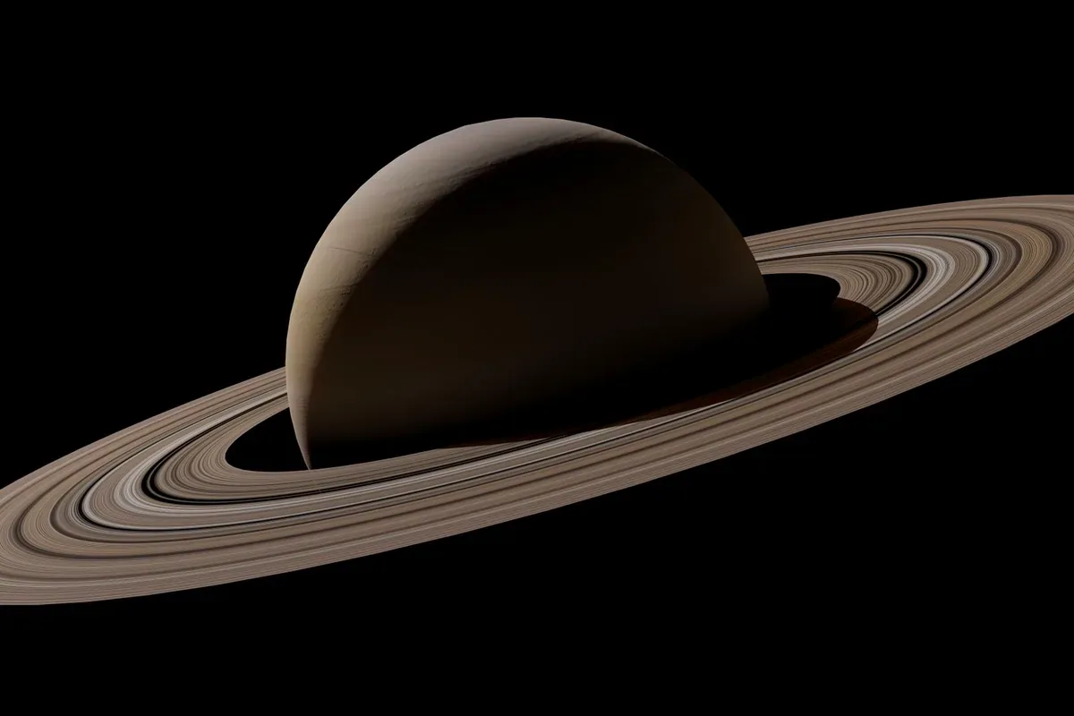 Saturno con sus anillos, iluminado de lado, sobre un fondo negro