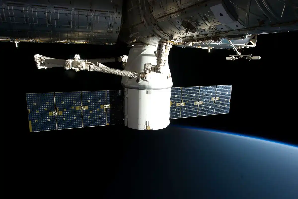 Brazo robótico de la Estación Espacial Internacional que sujeta una cápsula de carga sobre la Tierra