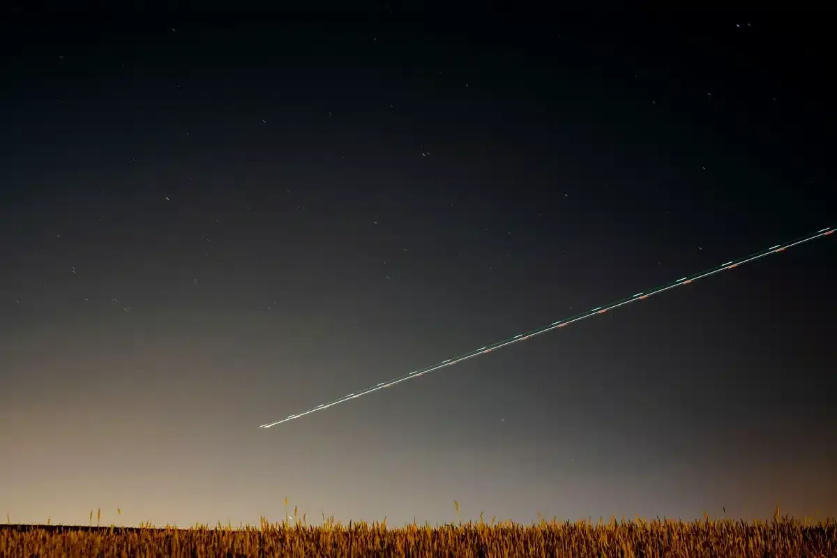 Trazo luminoso que cruza en diagonal un cielo nocturno sobre un campo