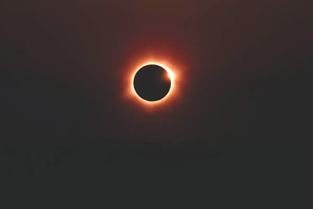 Eclipse solar total con un anillo de luz rojiza alrededor del disco oscuro de la Luna