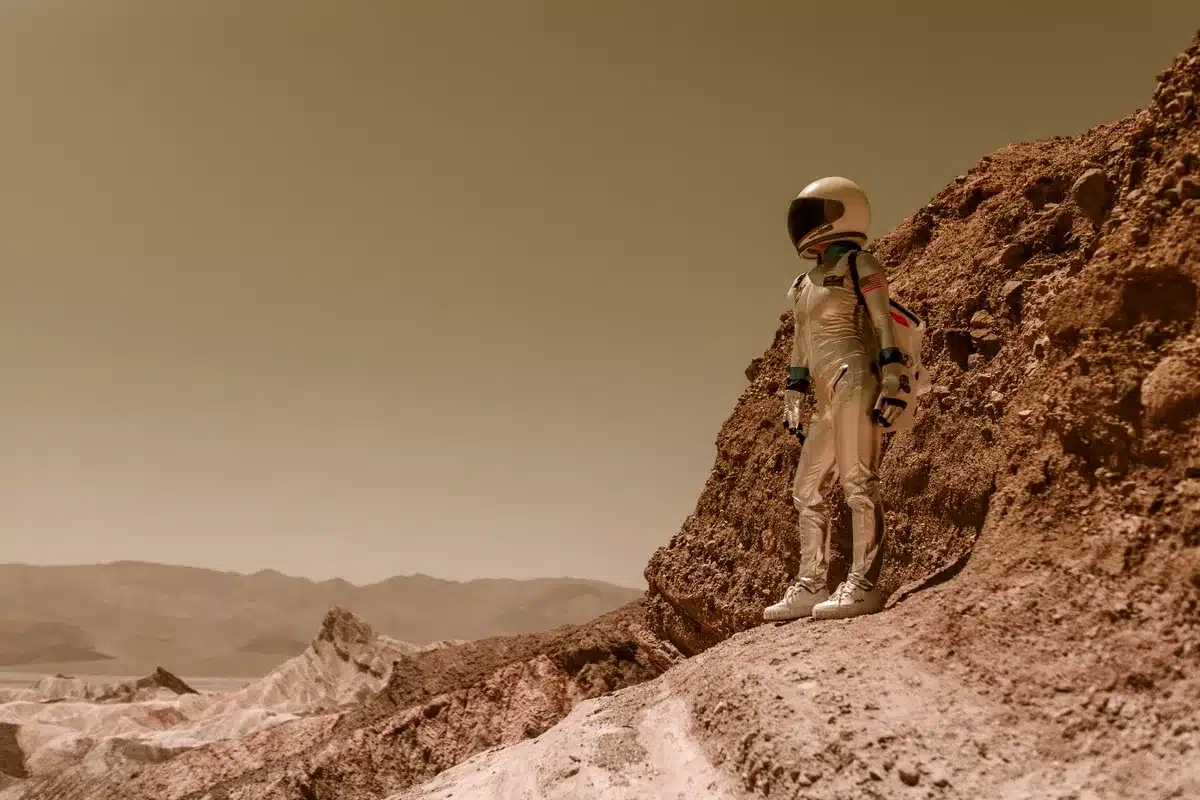 Astronauta de pie sobre una ladera rocosa en un paisaje desértico de tonos ocres