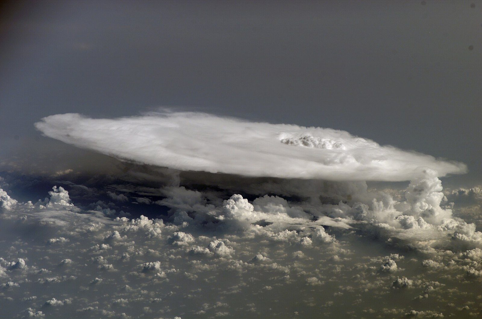 Nube cumulonimbo con forma de yunque extendida sobre un mar de nubes más pequeñas, vista desde arriba