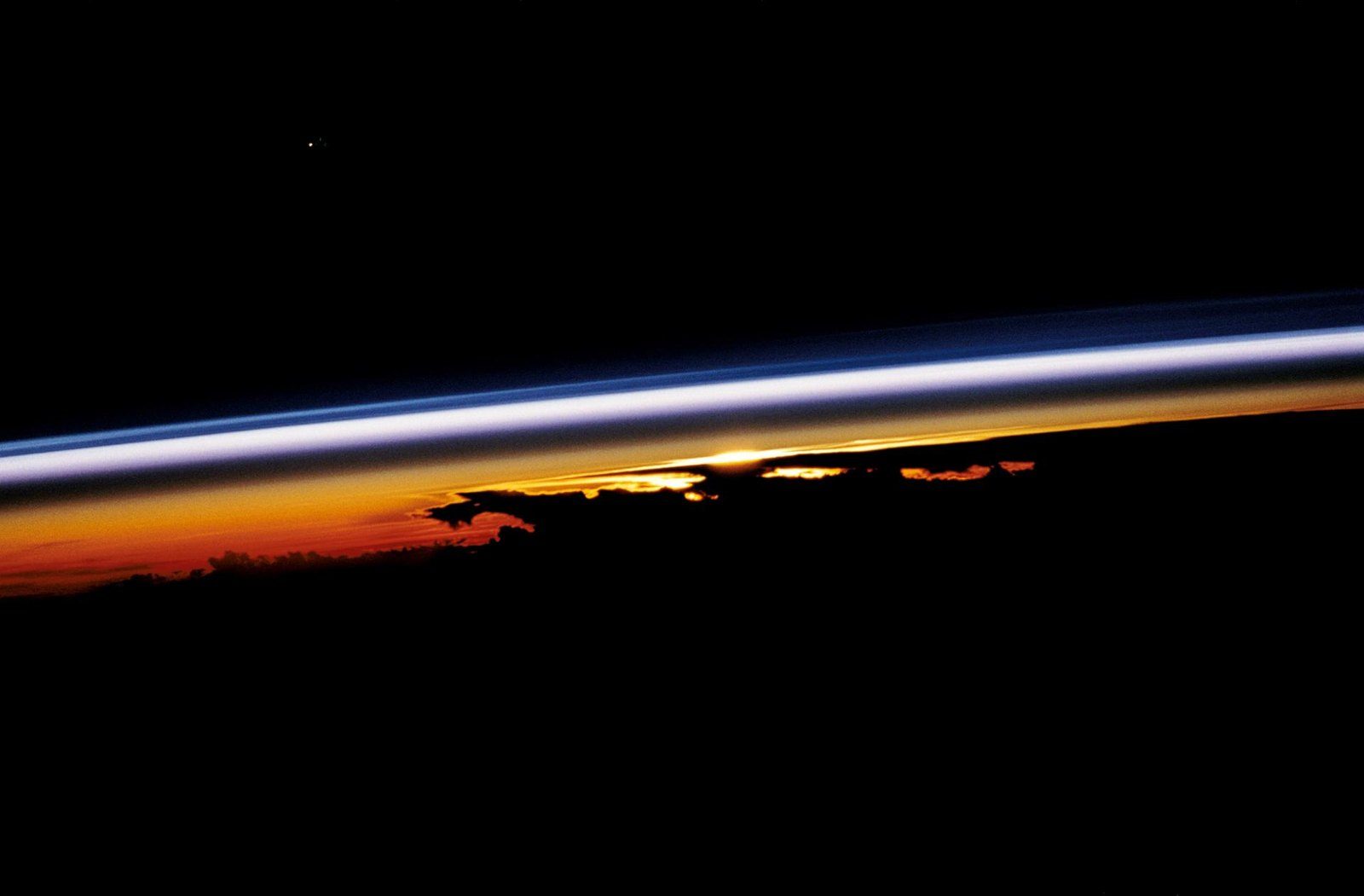 Amanecer visto desde el espacio con franjas de colores sobre el borde curvo de la Tierra y nubes recortadas contra la luz del Sol