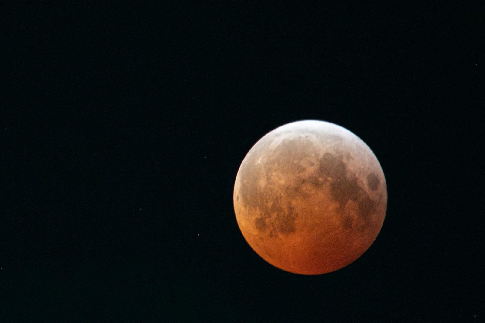 Luna llena en eclipse total, de tono naranja rojizo, con una franja clara en el borde superior, sobre un cielo negro con algunas estrellas