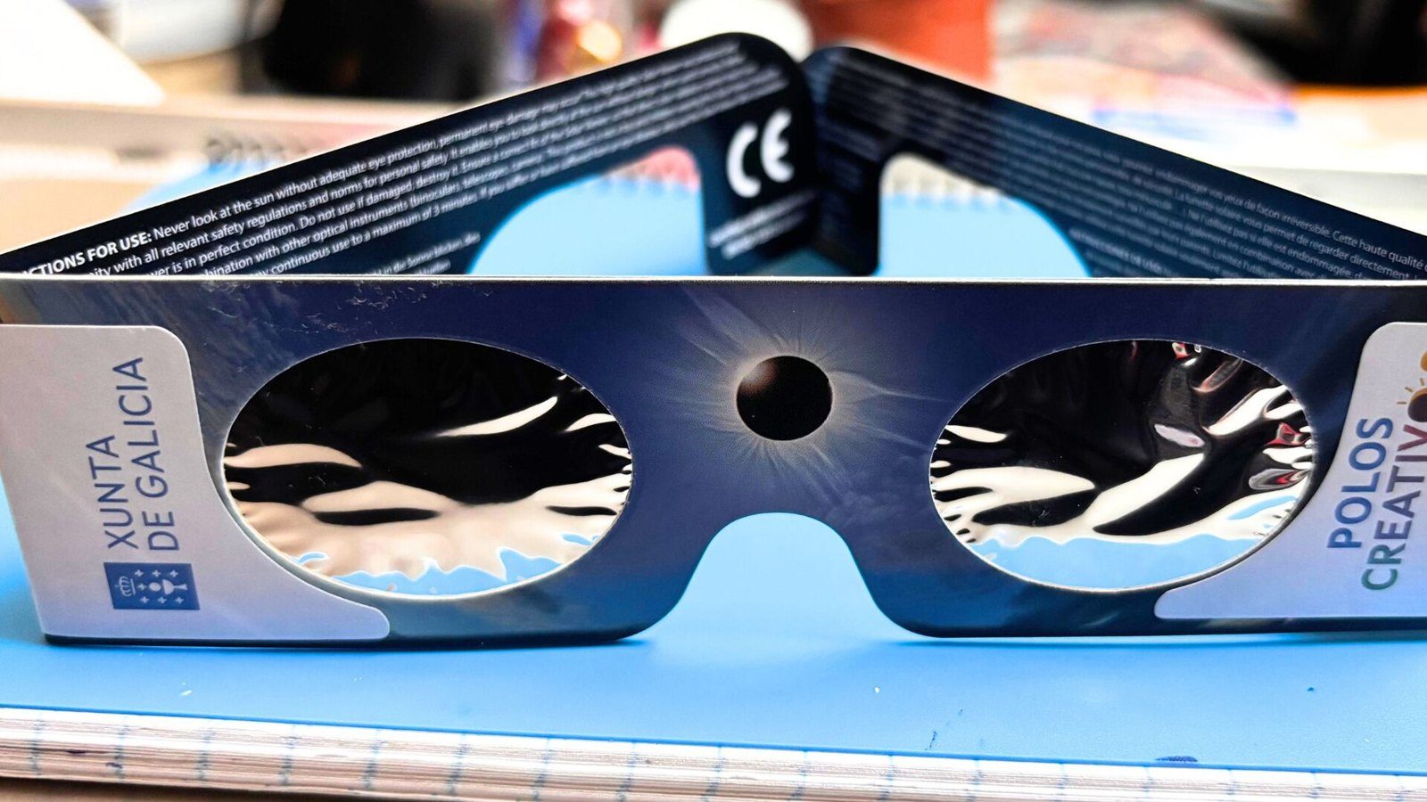 Gafas de cartón para observar eclipses, con filtros plateados y el marcado CE, sobre una superficie azul