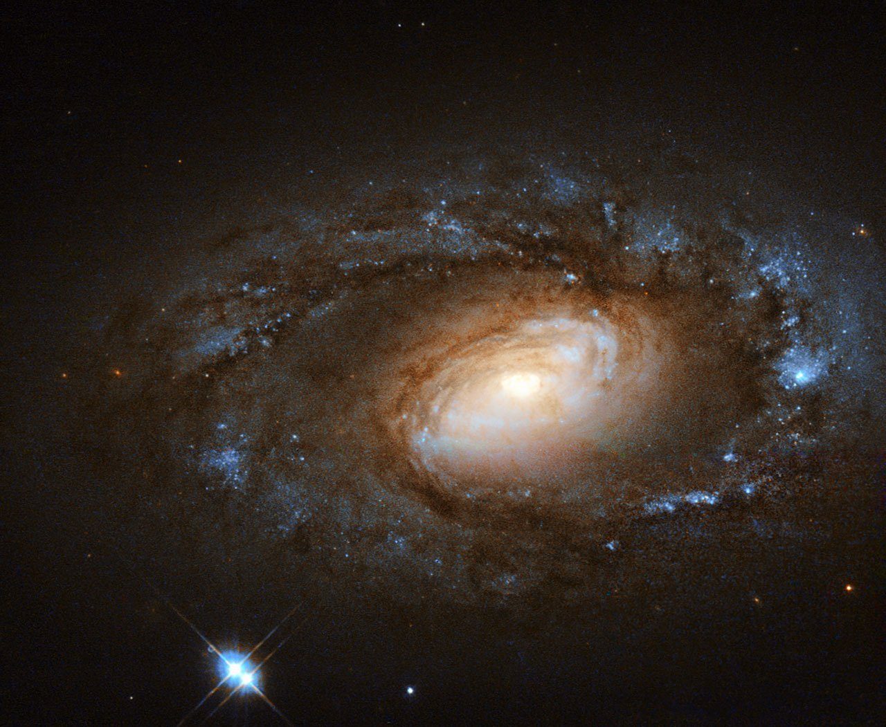 Galaxia espiral con un núcleo dorado brillante rodeado de brazos con polvo oscuro y cúmulos de estrellas jóvenes azules