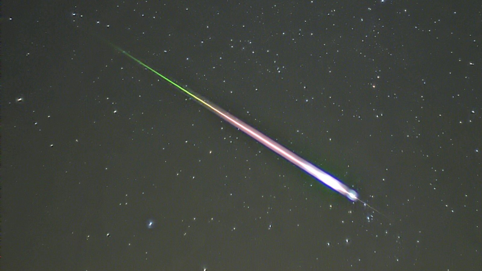 Un meteoro de las Leónidas deja un trazo verde y rosado entre las estrellas