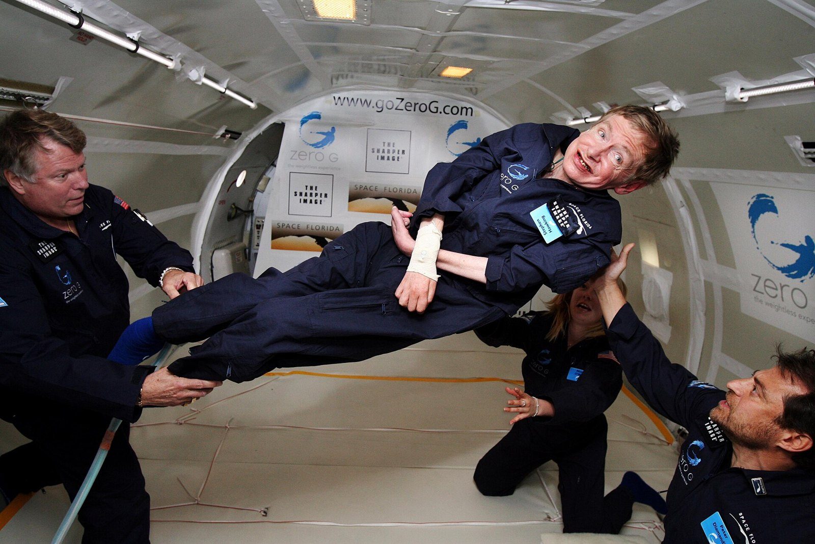Stephen Hawking flotando en ingravidez dentro de un avión, rodeado de varias personas que lo sostienen